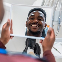 Dental patient’s smiling face reflected in handheld mirror
