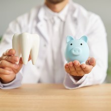 Dentist in white coat holding model tooth and blue piggy bank