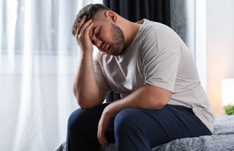 A depressed man sitting on a bed in his home